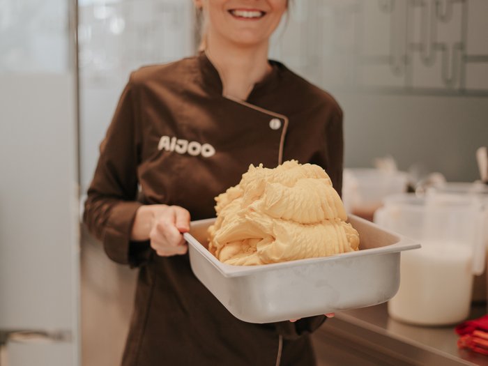 "Gambero Rosso": premiata la gelateria AiJOO Donna in uniforme marrone tiene un contenitore con gelato appena fatto