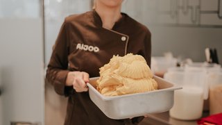 News Frau in brauner Arbeitskleidung hält Behälter mit frisch zubereitetem Gelato