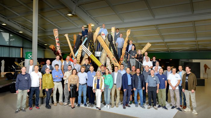 Nachbericht UNIKA Kunstmesse 2024 Gruppenfoto vor Kunstinstallation aus großen Holzskulpturen in Innenraum