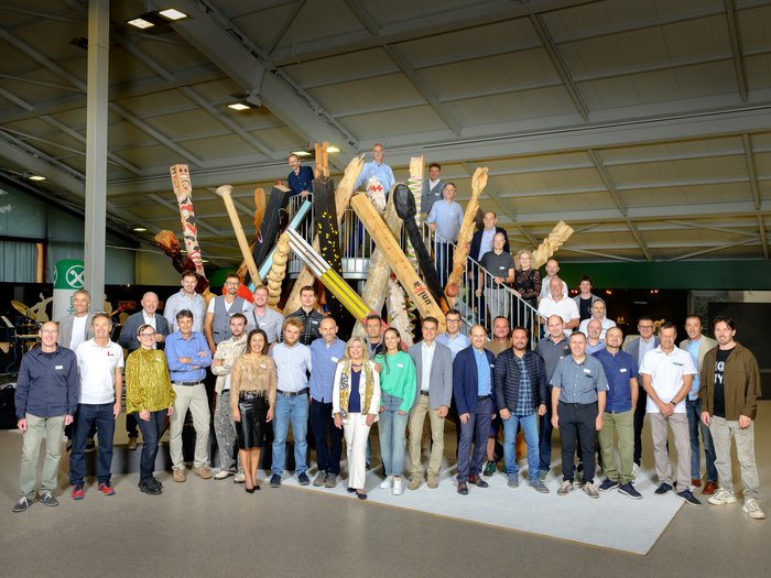 Nachbericht UNIKA Kunstmesse 2024 Gruppenfoto vor Kunstinstallation aus großen Holzskulpturen in Innenraum