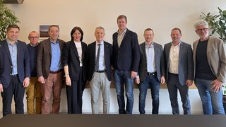 News Dieci professionisti in piedi sorridenti davanti a una parete in ufficio