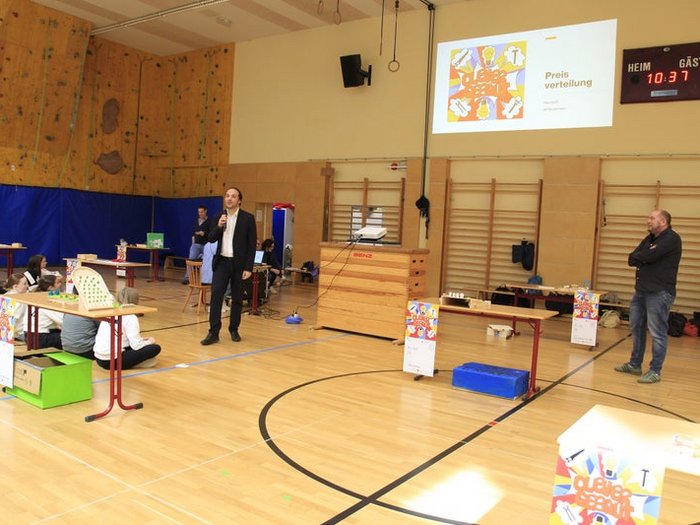 Kreative Spielideen: Preisverleihung für "Clever gebaut" Präsentation in Turnhalle mit Sprecher und Zuhörern