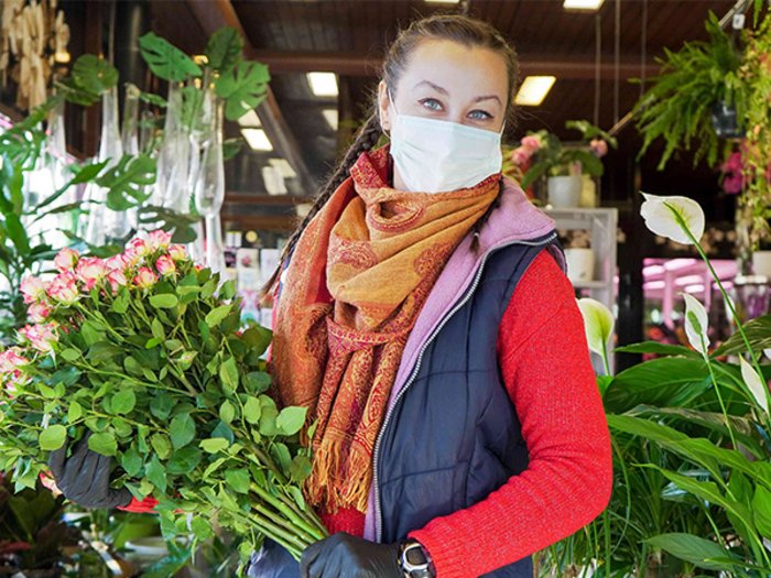 Valentinstag ist nicht abgesagt! Frau mit Maske hält Blumenstrauß in einer Blumenhandlung