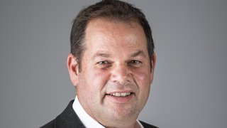 News Porträt eines Mannes mit grauem Anzug und weißem Hemd vor grauem Hintergrund