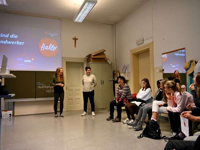 I giovani scoprono i mestieri nei settori dell’artigianato e dell’ospitalità Gruppo di persone in aula che ascolta una presentazione davanti a uno schermo