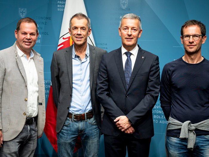 Riscaldare correttamente con la legna: lvh.apa e la Provincia lanciano la campagna di sensibilizzazione Quattro uomini davanti a bandiera e sfondo blu con scritte Provincia di Bolzano Alto Adige