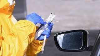 News Person in Schutzanzug und Handschuhen bereitet Abstrich für Covid-Test im Auto vor