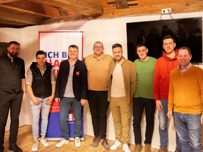 Zukunft ist Programm Acht Männer posieren lächelnd in einem Raum mit Holzdecke und Banner