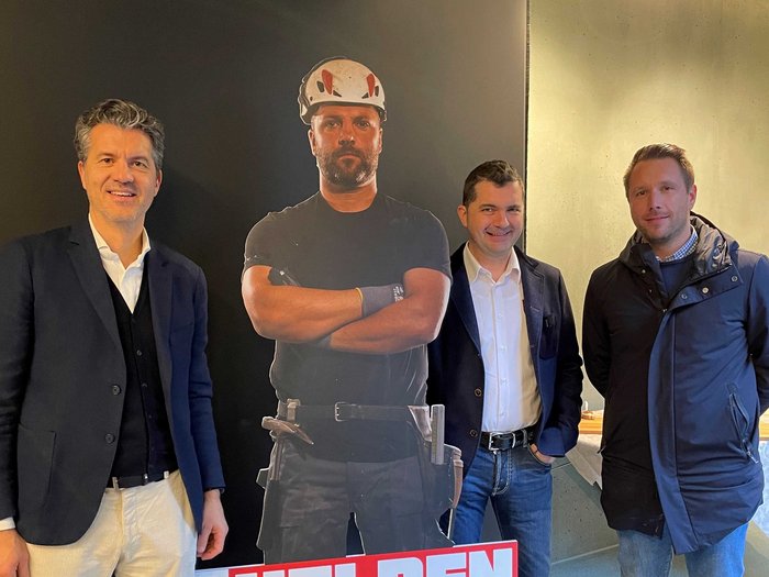 „Multitalent Beton“: ein voller Erfolg! Drei Männer stehen neben einer Baustellenhelden-Pappfigur mit Helm und Werkzeug