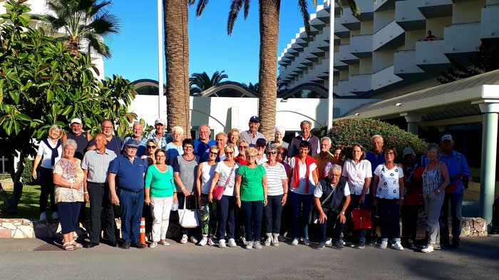 Althandwerker Rhodos 2022 © lvh.apa Große Gruppe älterer Menschen vor einem Hotel mit Palmen bei Sonnenschein