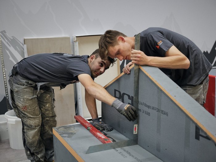 Südtirol begeistert beim Wettkampf der Fliesenleger/innen in Bozen! Zwei Handwerker messen und überprüfen ein Bauwerk mit Wasserwaage und Winkelmesser