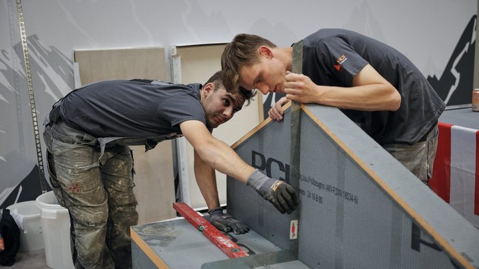Südtirol begeistert beim Wettkampf der Fliesenleger/innen in Bozen! Zwei Handwerker messen und überprüfen ein Bauwerk mit Wasserwaage und Winkelmesser
