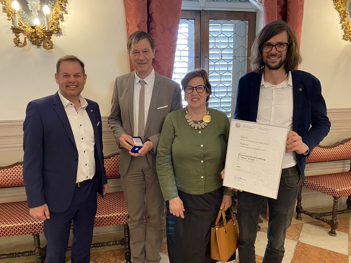 Verleihung des Südtiroler Wirtschaftspreises 2025 Vier Personen mit Urkunde und Medaille in einem historisch dekorierten Raum