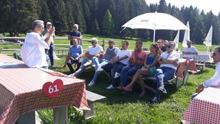 News Person spricht vor einer Gruppe im Freien bei sonnigem Wetter auf einer grünen Wiese