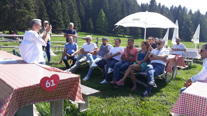 Dachdecker leben Gemeinschaft vor Person spricht vor einer Gruppe im Freien bei sonnigem Wetter auf einer grünen Wiese