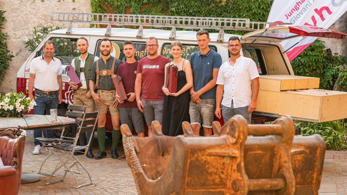 lvh-Vizepräsident Hannes Mussak, Norman Ventura, Thomas Ventura, Elias Thomaser, Lorenz Taber, Johanna Zacher, Jakob Zacher und Alexander Dallio. © KRAiTL_Photographie Gruppe von acht jungen Handwerkern vor einem Fahrzeug und Baggerlöffel