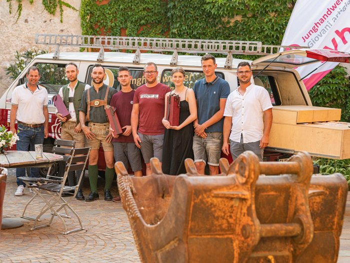 I Giovani Artigiani e la passione per i mestieri tradizionali Gruppo di otto giovani artigiani davanti a un veicolo e una benna da scavo