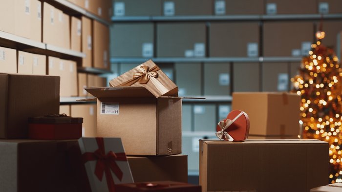 „Kein Interesse an gelenkter Lieferverzögerung“ Weihnachtsgeschenke in Kartons im Lager mit Weihnachtsbaum im Hintergrund.