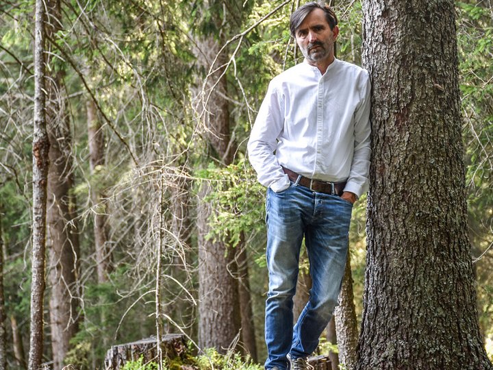 Falegnameria Reinhold Stoll Uomo appoggiato a un albero in una foresta con camicia bianca e jeans