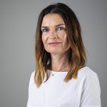 Das lvh-Team Porträt einer Frau mit braunem Haar und weißem Oberteil vor grauem Hintergrund