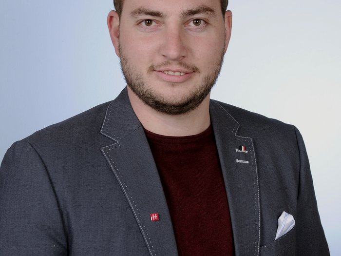 Importanti investimenti nel settore delle costruzioni Ritratto di un uomo giovane con giacca grigia e maglione rosso su sfondo chiaro