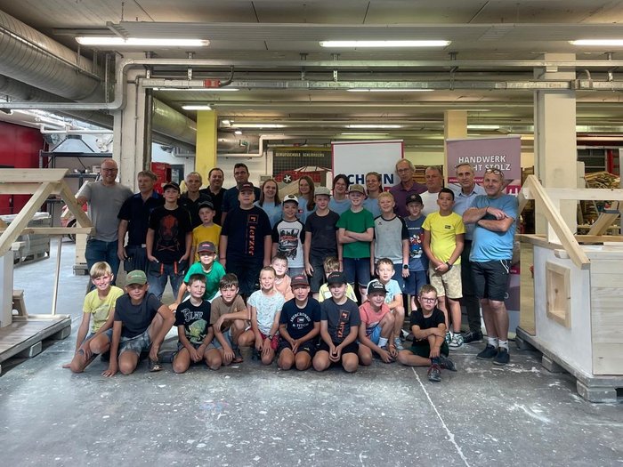 Kids Academy des lvh: 48 Kinder entdecken die Welt des Handwerks Gruppenfoto von Kindern und Erwachsenen in einer Werkstatt mit Holzprojekten