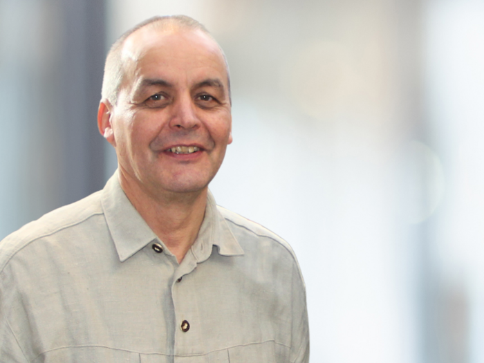 Fondo per le costruzioni in legno: la tutela del clima incontra l’artigianato Uomo con camicia grigia che sorride davanti a sfondo sfocato