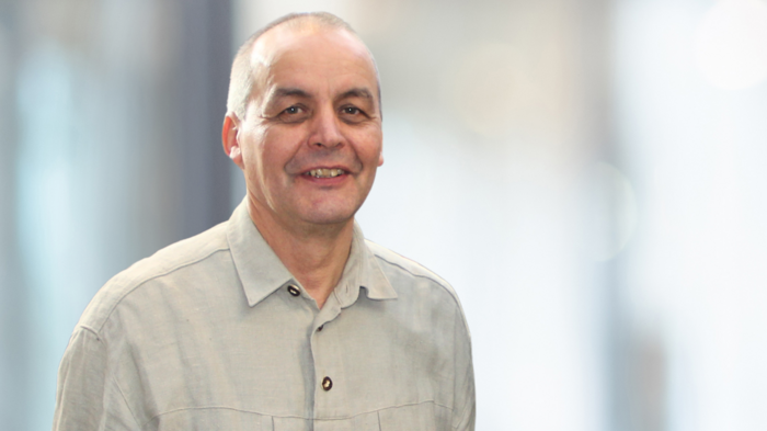 Holzbaufonds: Klimaschutz trifft Handwerk Mann mit grauem Hemd lächelnd vor unscharfem Hintergrund