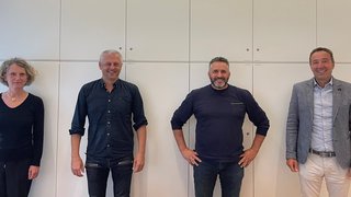 News Vier lächelnde Personen stehen vor einer weißen Wand