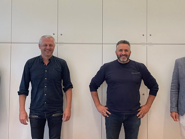 Una collaborazione di valore verso obiettivi comuni Quattro persone sorridenti in piedi davanti a una parete bianca