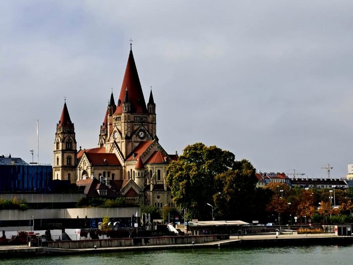 Auf Reisen: Althandwerker auf Flusskreuzfahrt Blick auf Kirche mit roten Türmen am Flussufer unter bewölktem Himmel
