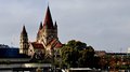 Auf Reisen: Althandwerker auf Flusskreuzfahrt Blick auf Kirche mit roten Türmen am Flussufer unter bewölktem Himmel