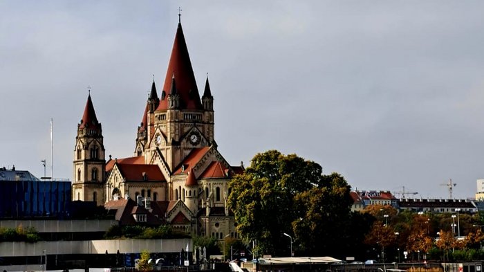 Auf Reisen: Althandwerker auf Flusskreuzfahrt Blick auf Kirche mit roten Türmen am Flussufer unter bewölktem Himmel