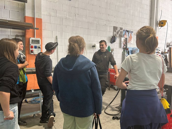 Entdeckungsreise in Berufe des Handwerks und Gastgewerbes an der Mittelschule St. Martin in Passeier Gruppe junger Menschen in Werkstatt beim Zuhören einer Person