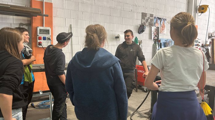 Entdeckungsreise in Berufe des Handwerks und Gastgewerbes an der Mittelschule St. Martin in Passeier Gruppe junger Menschen in Werkstatt beim Zuhören einer Person