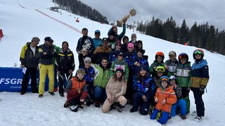 News Gruppenfoto von Skifahrern und Trainern mit Trophäen im Schnee vor einem Skihang