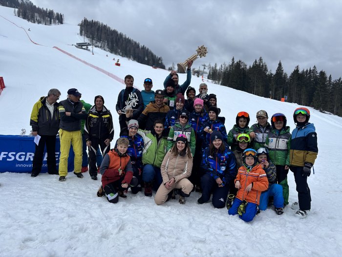 Handwerker/innen tauschen Werkzeuge gegen Skier und Rodel Gruppenfoto von Skifahrern und Trainern mit Trophäen im Schnee vor einem Skihang