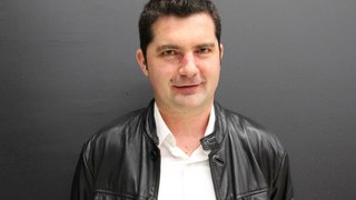 News Porträt eines Mannes mit schwarzer Lederjacke und weißem Hemd vor grauem Hintergrund