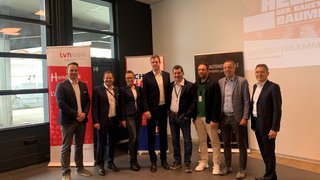 News Gruppe von acht Personen bei einer Veranstaltung vor Bannern im Innenraum