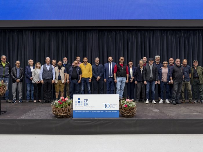 Bauarbeiterkasse der Autonomen Provinz Bozen: Ehrung der Mitglieder „30 Jahre Vertrauen“ Gruppenfoto von 22 Personen auf Bühne vor CE BK 30 Jahre Vertrauensschild