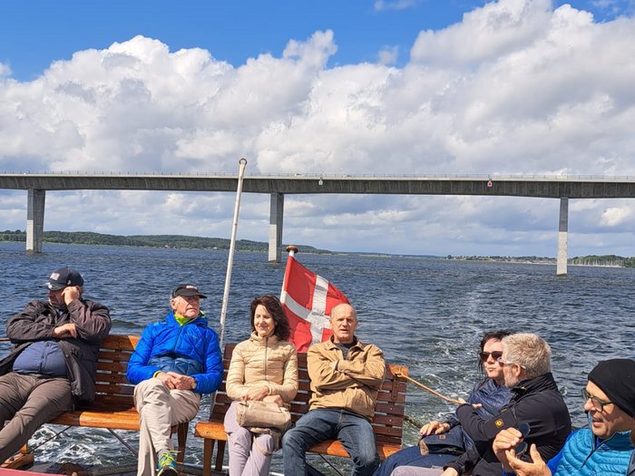 Reisefreudige Althandwerker/innen Gruppenfoto von Menschen auf einem Boot mit einer Brücke im Hintergrund und dänischer Flagge