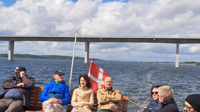 Reisefreudige Althandwerker/innen Gruppenfoto von Menschen auf einem Boot mit einer Brücke im Hintergrund und dänischer Flagge