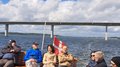 Reisefreudige Althandwerker/innen Gruppenfoto von Menschen auf einem Boot mit einer Brücke im Hintergrund und dänischer Flagge