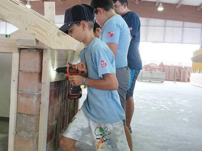 Kids-Academy 2024: buntes Handwerk in Bruneck Jugendliche bohren Löcher in Holzrahmen bei einem Werkstattprojekt