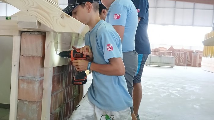 Kids-Academy 2024: buntes Handwerk in Bruneck Jugendliche bohren Löcher in Holzrahmen bei einem Werkstattprojekt