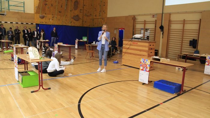 Kreative Spielideen: Preisverleihung für "Clever gebaut" Frau spricht in Sporthalle vor sitzenden und stehenden Zuhörern