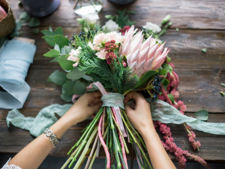 Fioristi Mani che legano un bouquet di fiori rosa e foglie verdi su un tavolo di legno