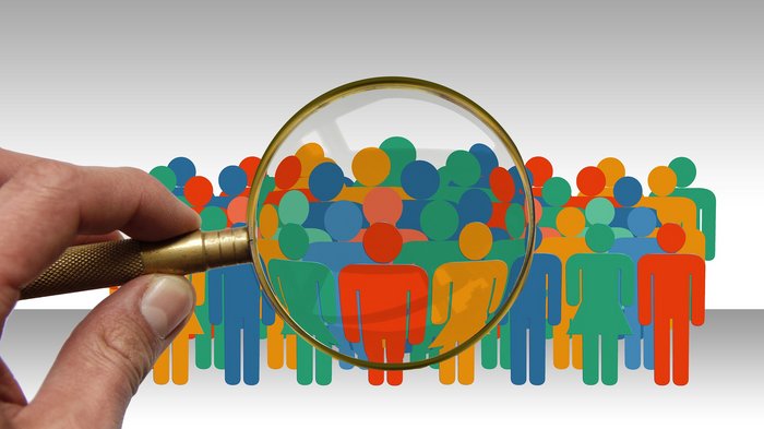 „Besonderheiten der Branchen sollen im Vordergrund stehen“ Lupe fokussiert auf bunte Piktogramme von Menschen in einer Menschenmenge
