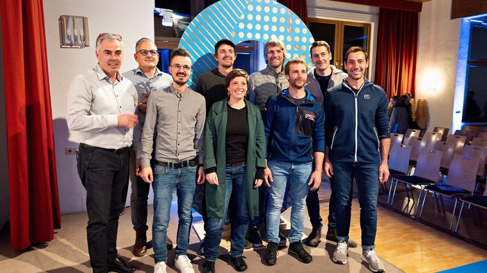 Rittner Musterschau verbindet Menschen und Ideen Neun Personen posieren in einem Raum mit Stühlen und rotem Vorhang für ein Gruppenfoto