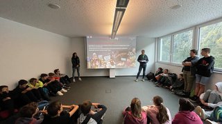 © Mitteschule Pankraz und Ulten Jugendliche sitzen im Kreis und hören einem Vortragenden im hellen Klassenraum zu